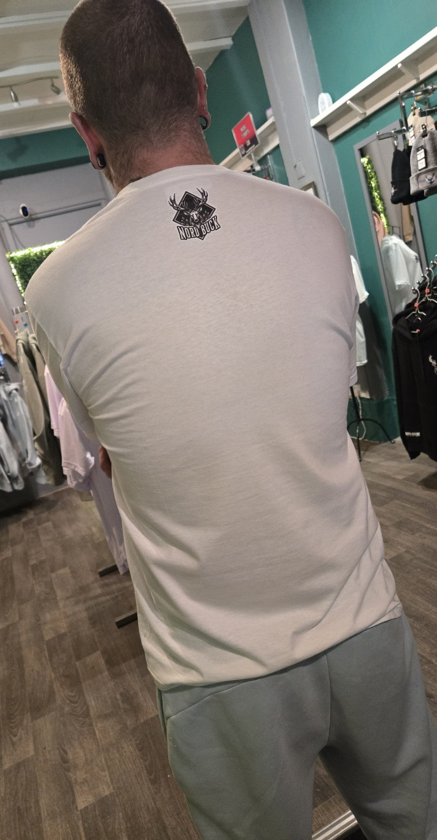 Person wearing a light gray t-shirt with a logo on the back in a store setting.