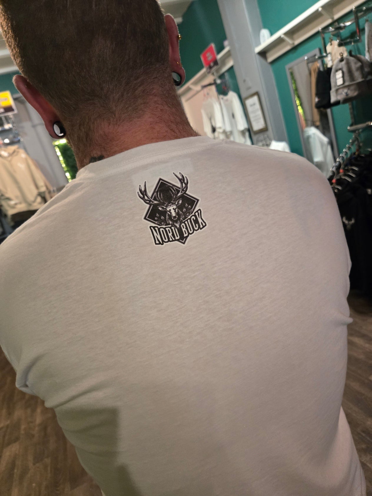 Person wearing a white t-shirt with a black logo on the back, standing in an industrial setting.