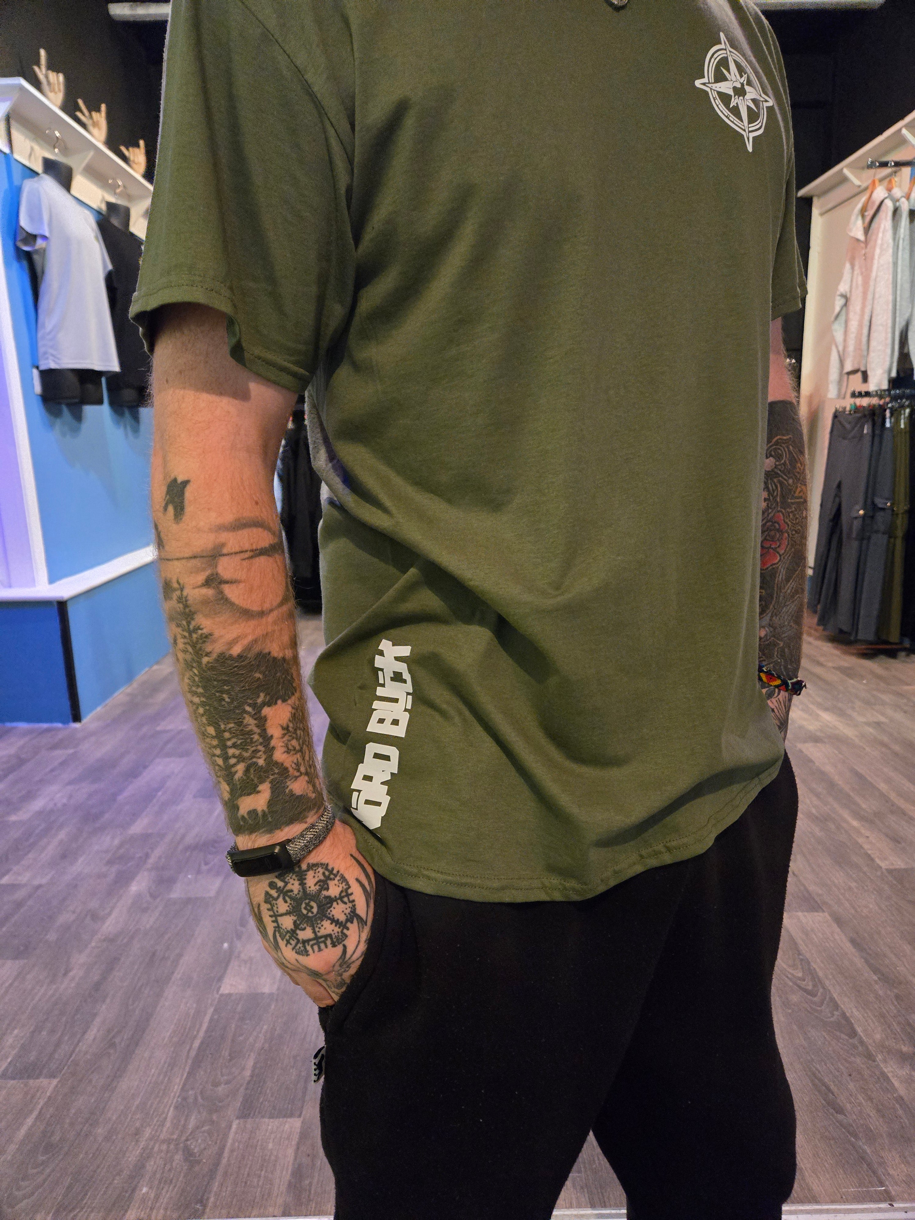 Person wearing a green top with text on the bottom, standing indoors.