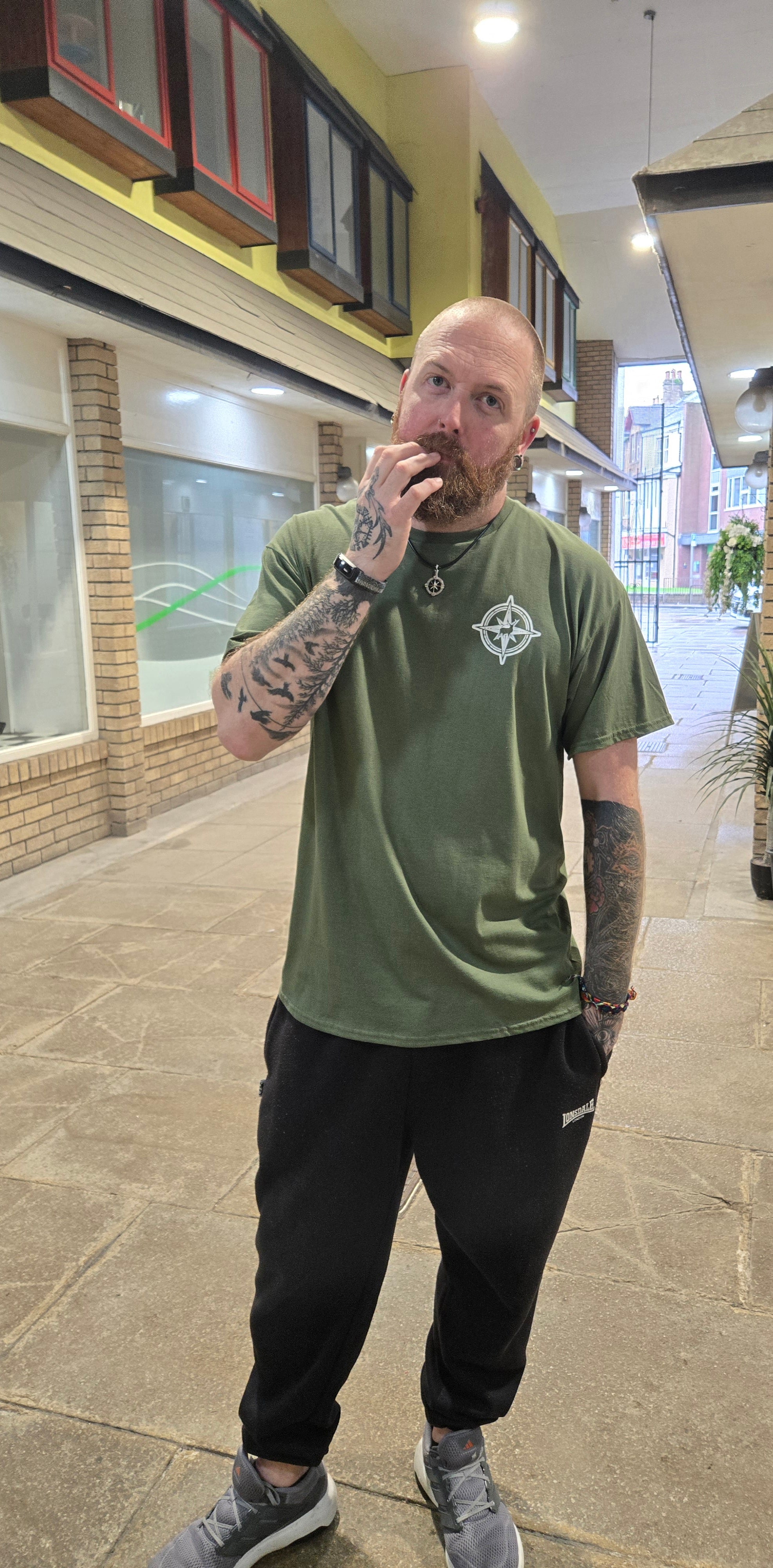 Man in a green t-shirt and black pants standing in a mall.