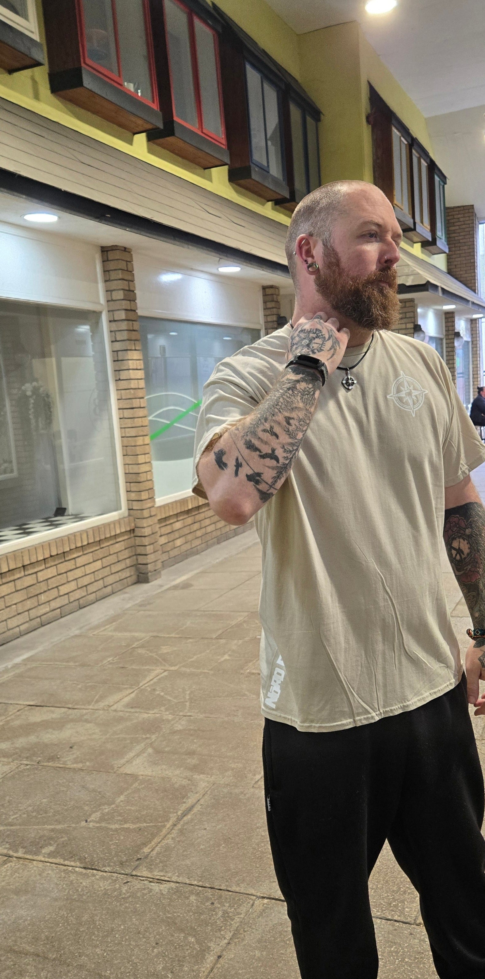 Man with tattoos standing on a sidewalk in an urban setting