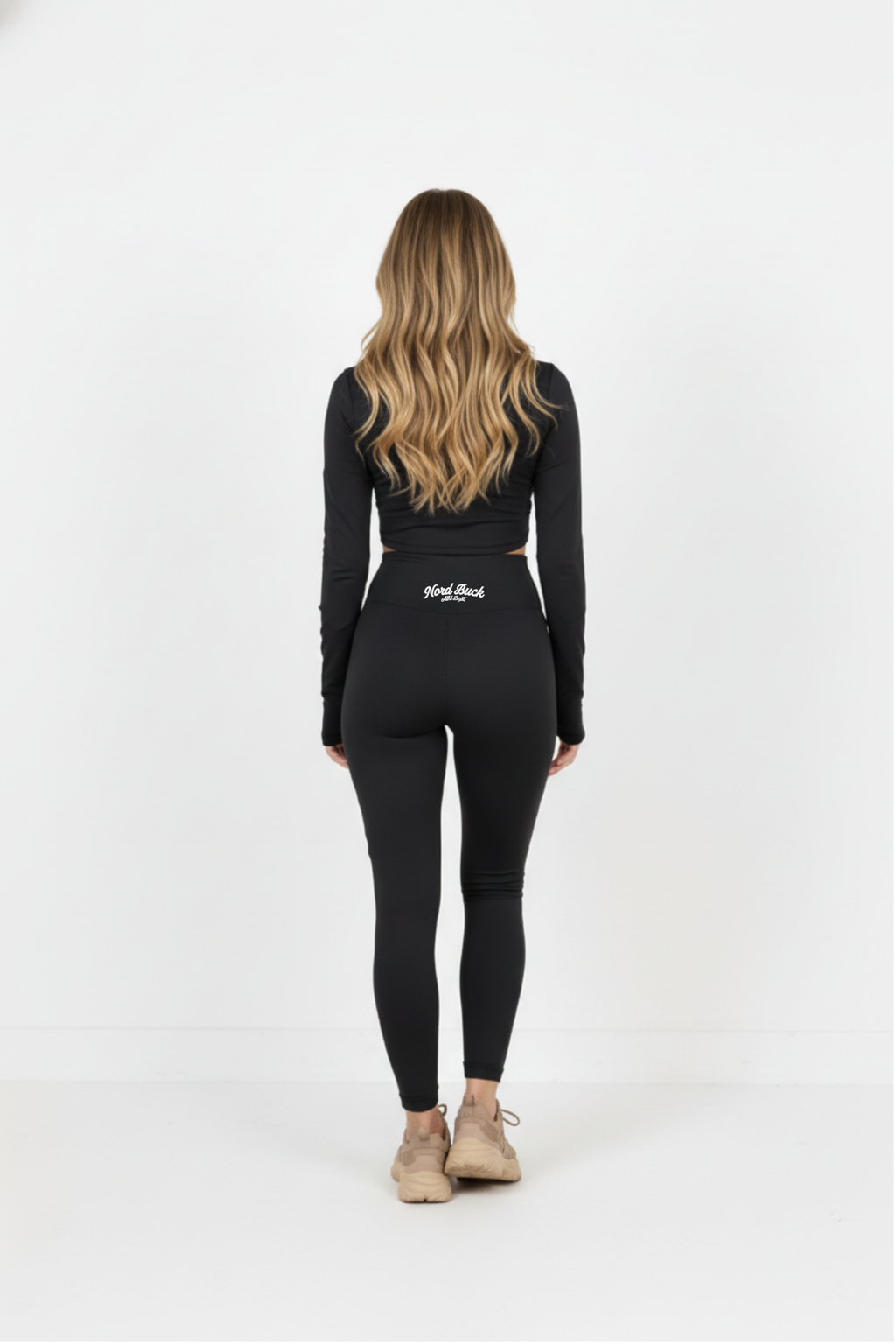 Person wearing a black long-sleeve top and leggings with a logo on a white background