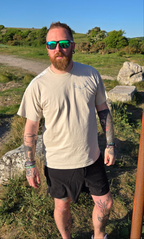 man standing wearing beige tshirt with stag on, on the beach