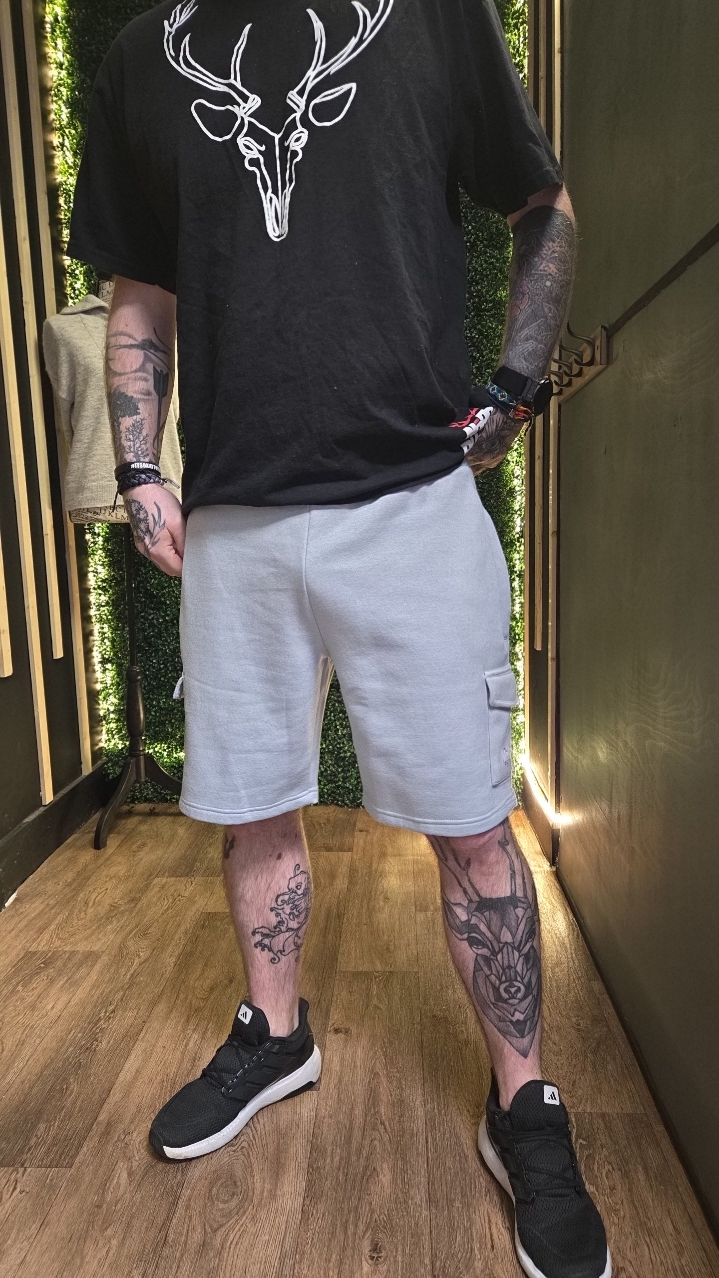 Person wearing a black t-shirt with a white deer design and light gray shorts indoors.