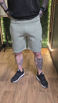 Person wearing light gray shorts and black sneakers on a wooden floor with greenery in the background