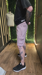 Person wearing a black t-shirt, light Lavender shorts, and black sneakers with tattoos on arms and legs in a store setting.