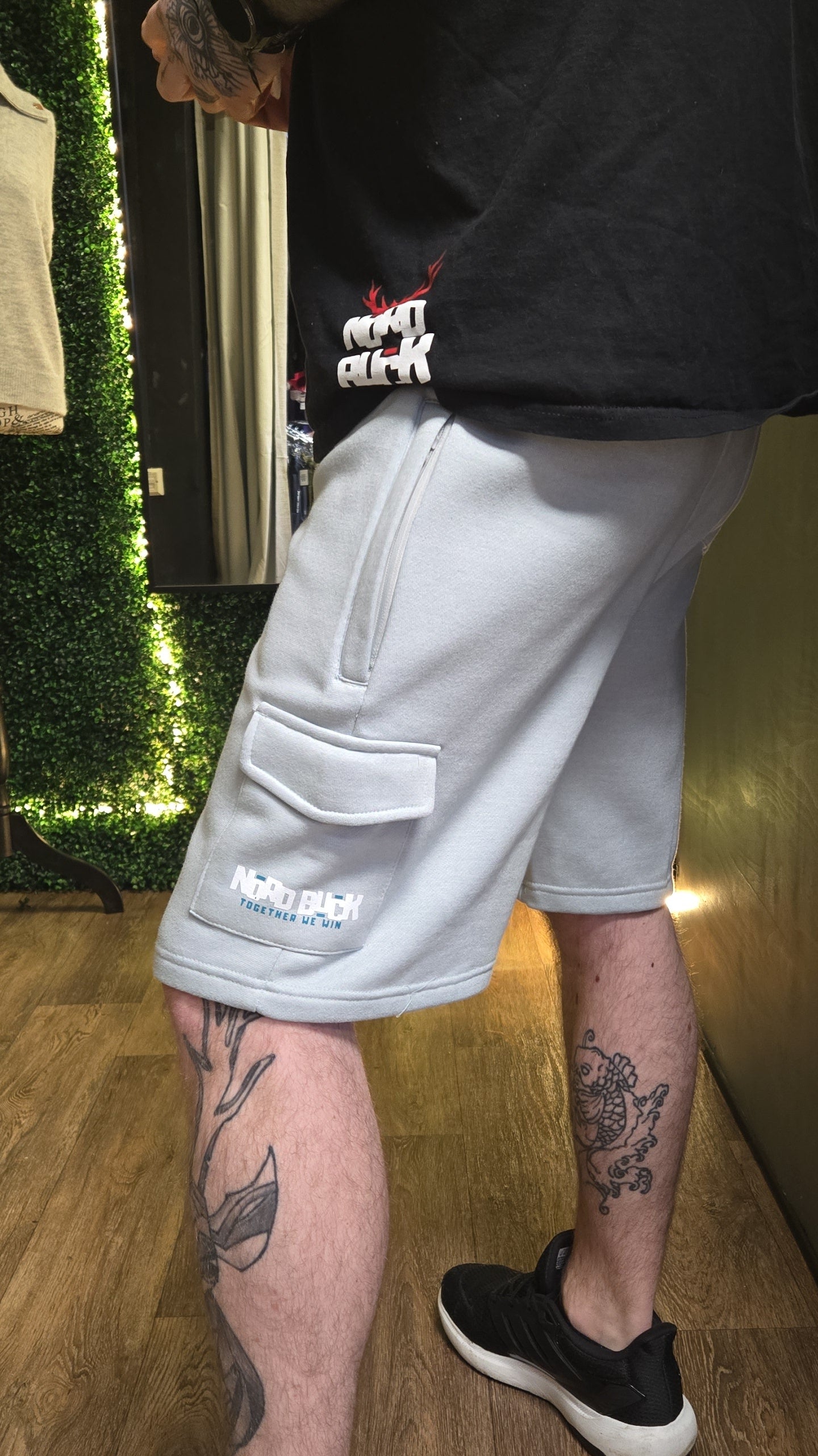 Person wearing light gray shorts with branding, standing indoors.