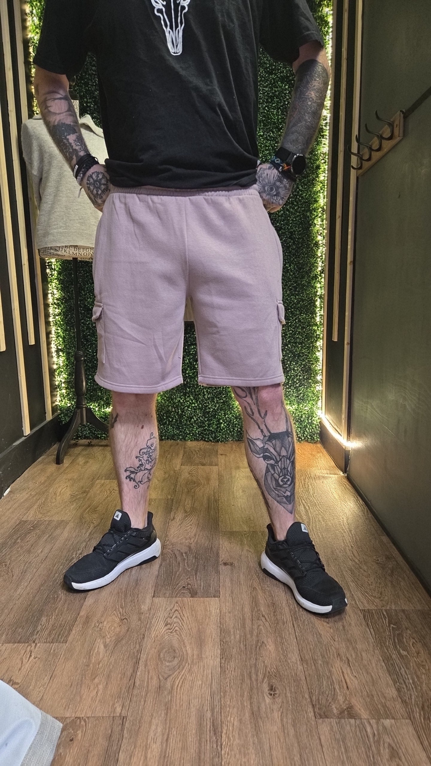 Person wearing a black t-shirt, light purple cargo shorts, and black sneakers with tattoos on arms and legs.