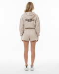 Person wearing a beige hoodie and shorts set with 'Nora Buck' branding on a white background