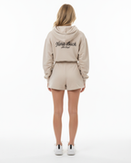 Person wearing a beige hoodie and shorts set with 'Nora Buck' branding on a white background