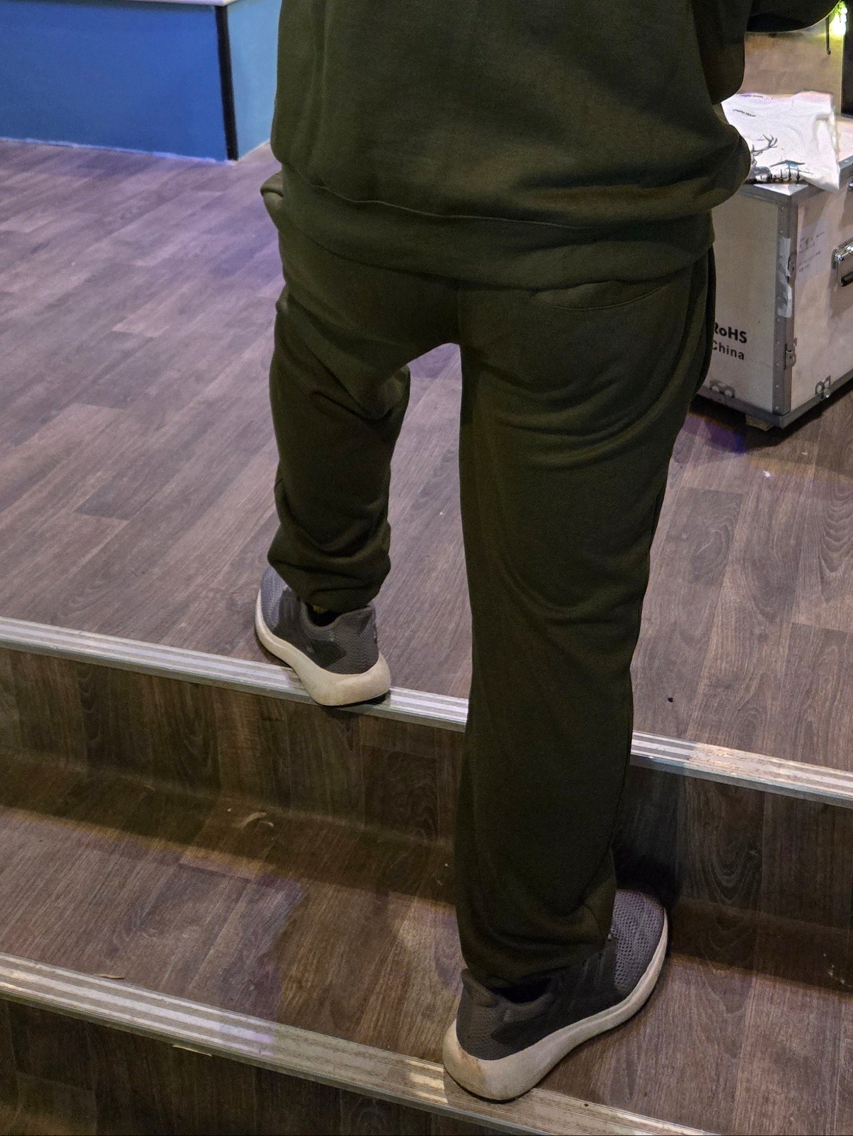 Person wearing a green jacket and dark pants standing on a reflective surface with a store interior in the background.