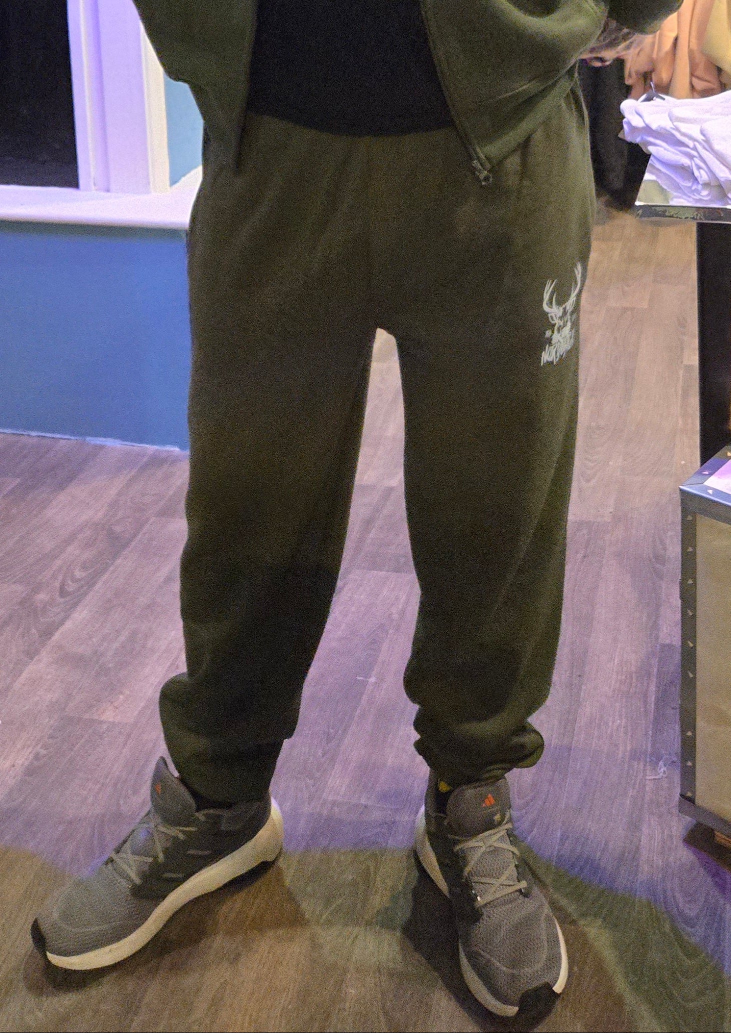 Man wearing a green tracksuit standing in a store with clothing and merchandise in the background.