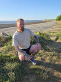 man kneeling down wearing beige tshirt with stag on, on the beach