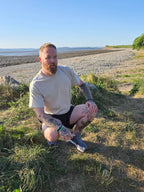 man kneeling down wearing beige tshirt with stag on, on the beach
