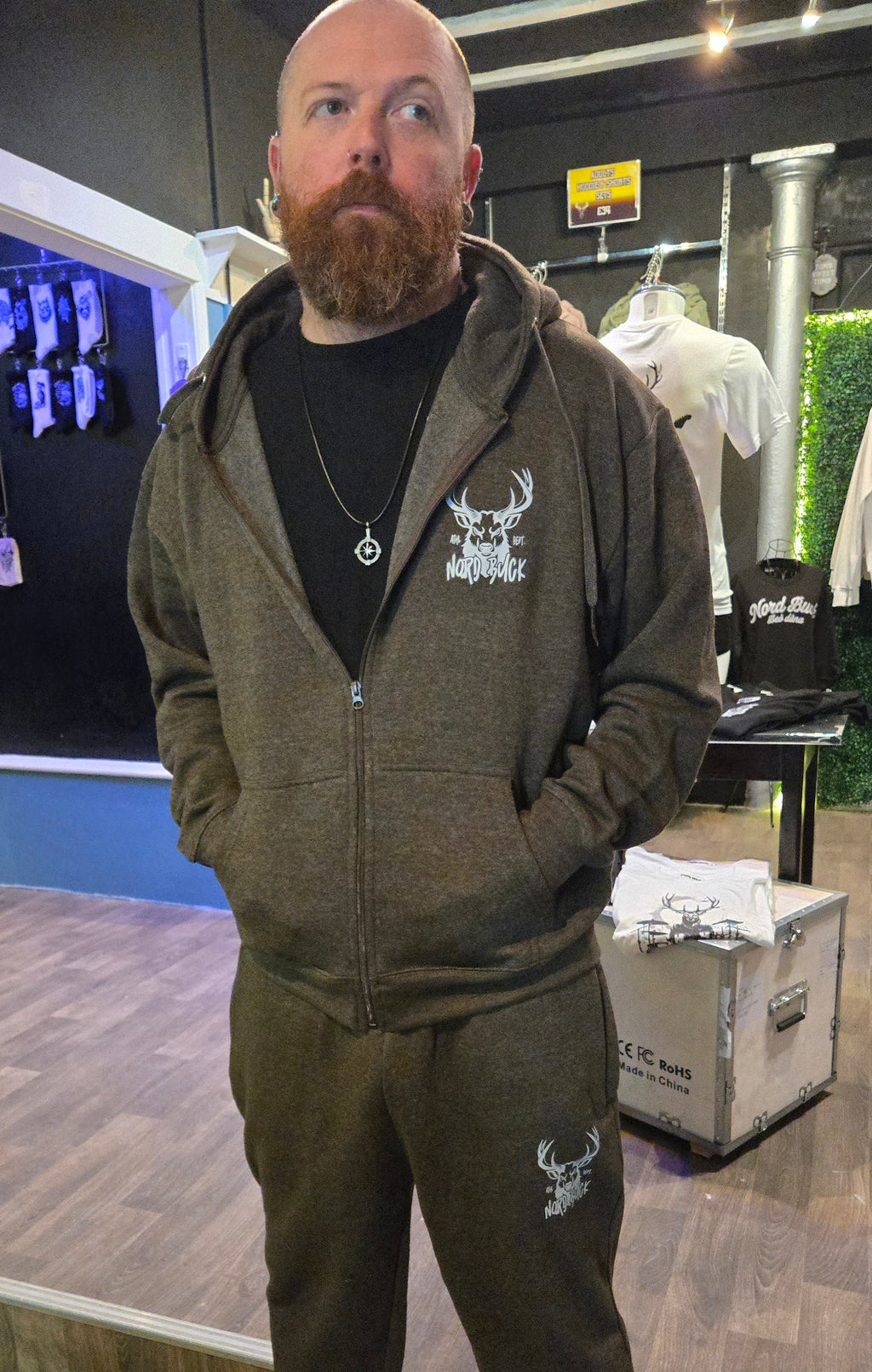 Man wearing a green hoodie and pants in a store setting with merchandise in the background.